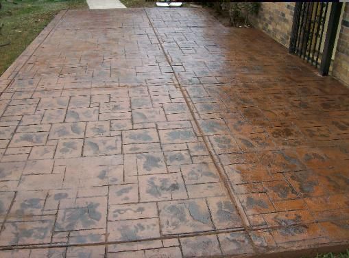 A concrete driveway with a brick pattern and a fence in the background.