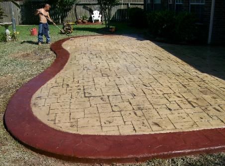 A man is painting a concrete patio with a red border.