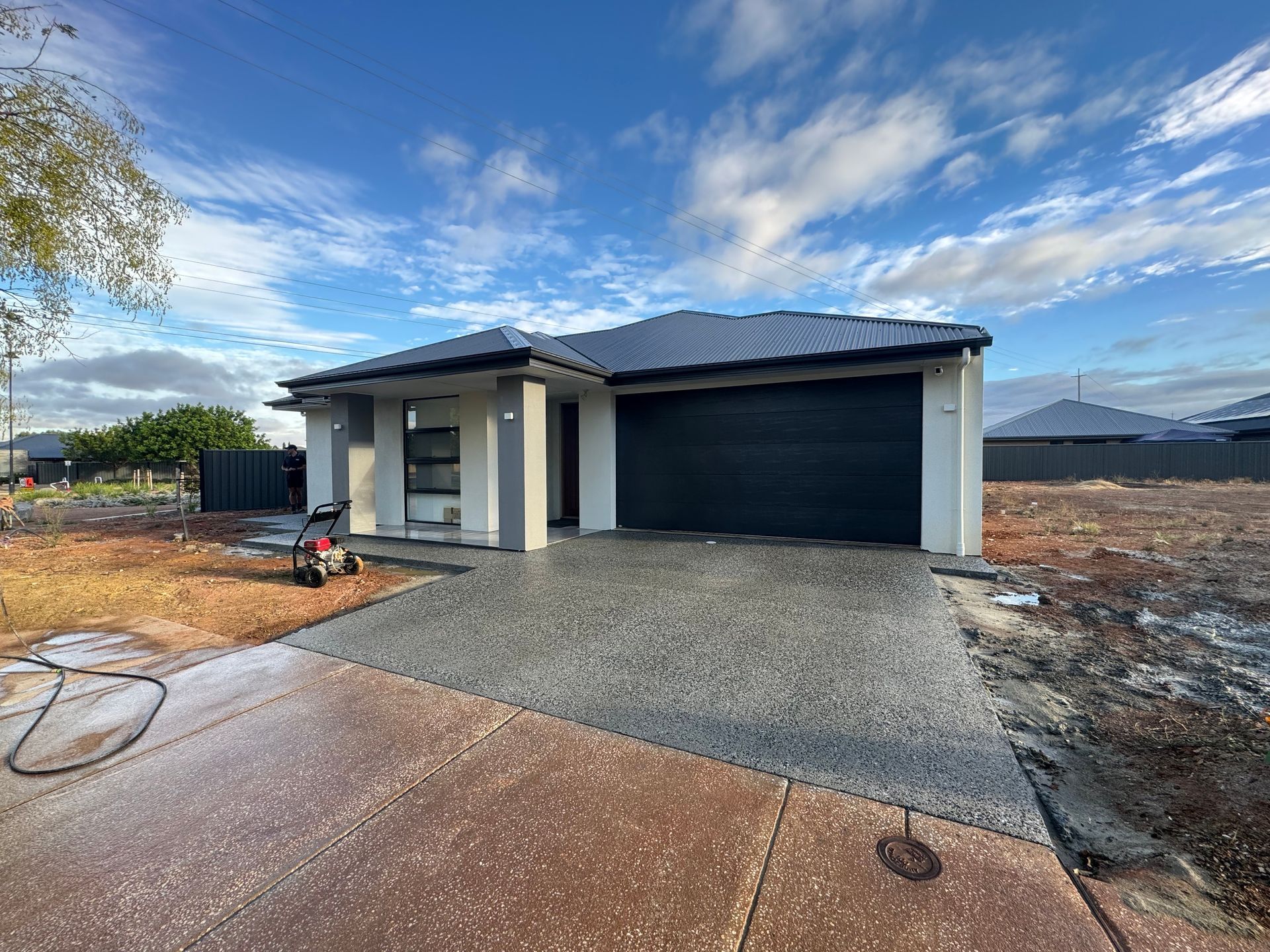 A house with a black garage door is sitting on top of a dirt field.