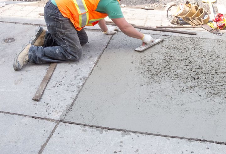 A construction worker is kneeling on the ground using a trowel