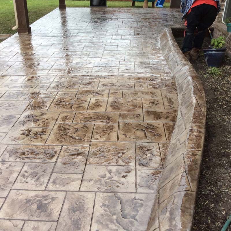 A person is working on a concrete patio with a hose