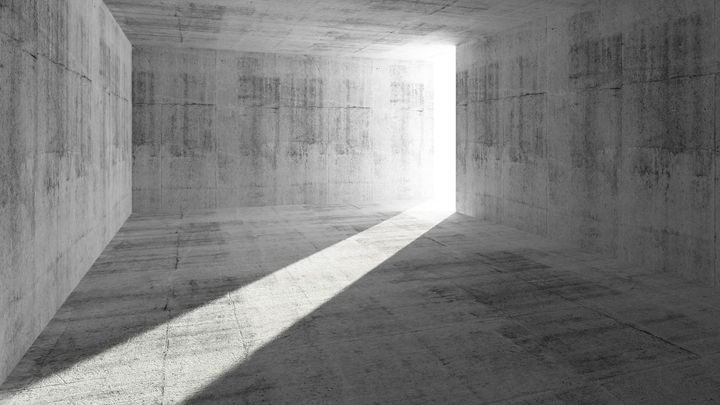 A light is shining through a doorway in a concrete room.