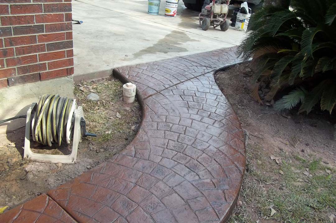 A hose is sitting on a concrete walkway next to a brick building.