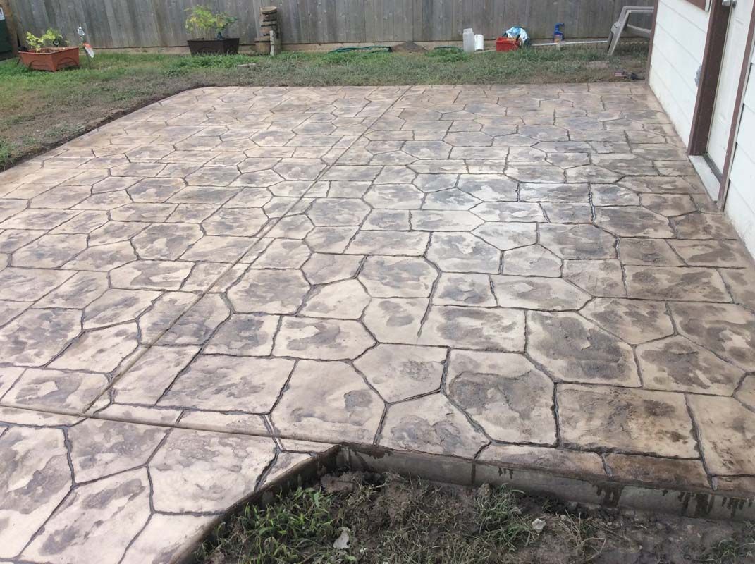 A concrete patio with a geometric pattern is in the backyard of a house.
