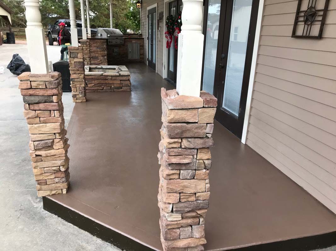 A porch with stone pillars and a concrete floor