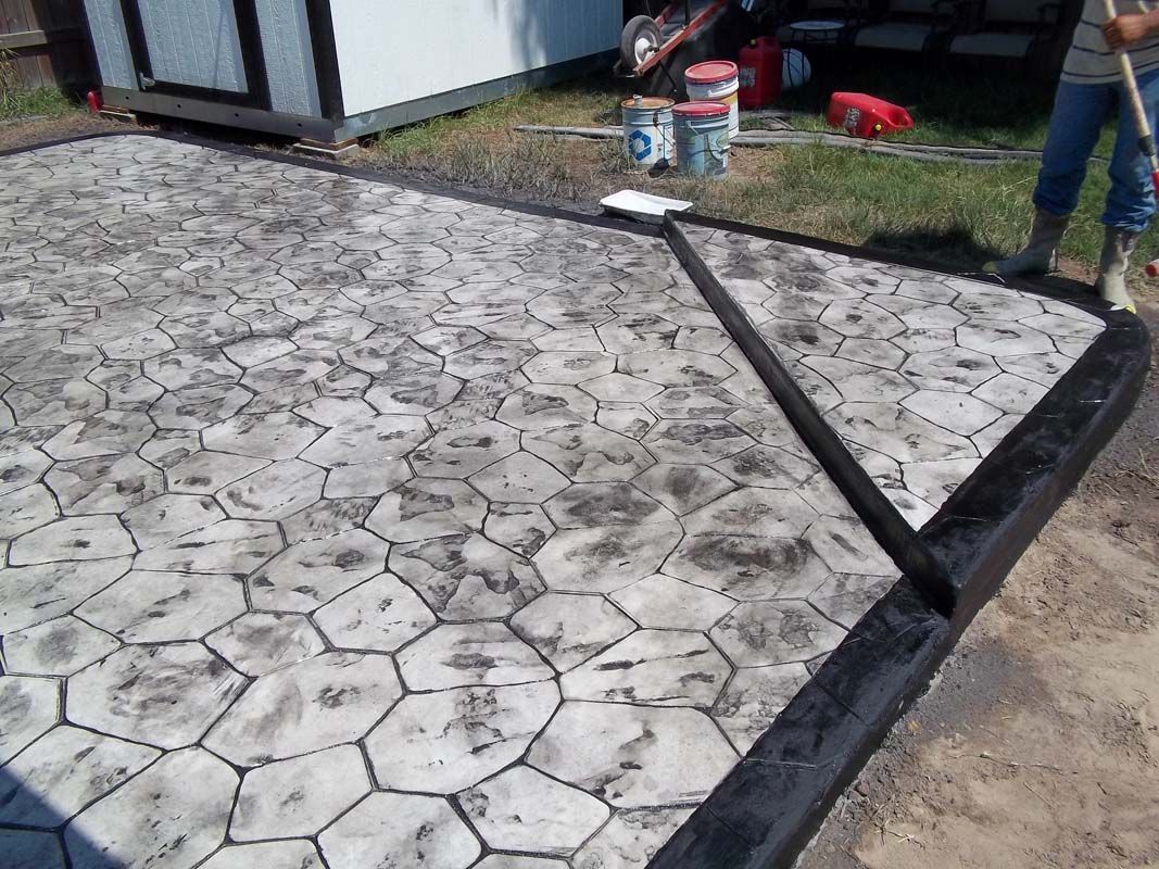 A person is painting a concrete driveway with a broom.