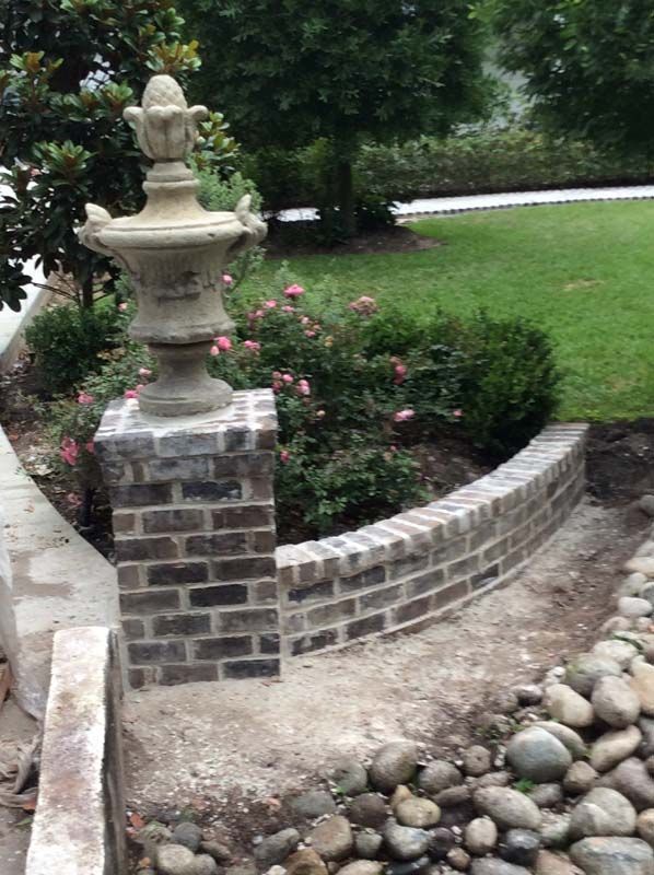 A stone fountain is sitting on top of a brick wall in a garden.
