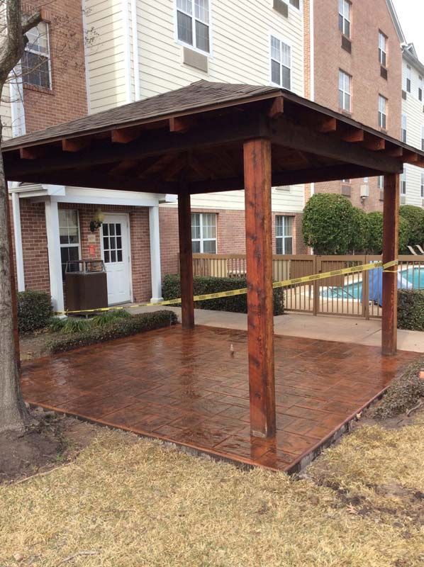 A wooden gazebo is sitting in front of a building next to a pool.