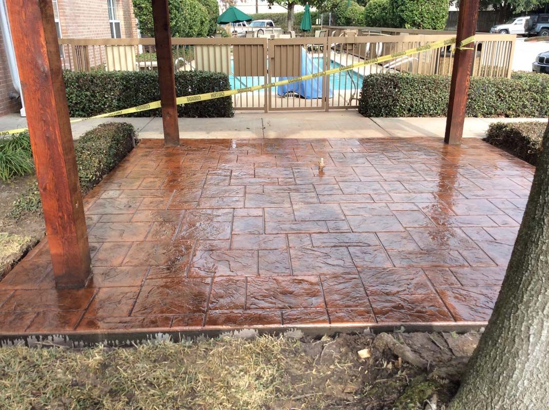 A patio with a wooden pergola and a pool in the background.