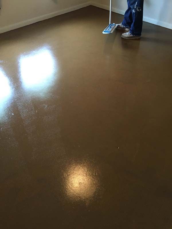 A person is mopping a brown floor with a mop.