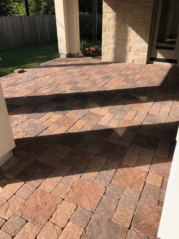 A brick patio with steps leading up to it and a fence in the background.