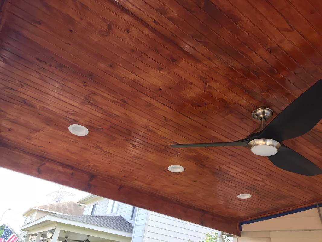 A ceiling fan is hanging from the ceiling of a wooden porch.