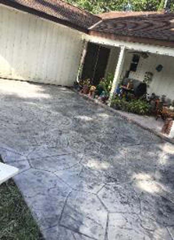 A concrete driveway in front of a house with a porch.