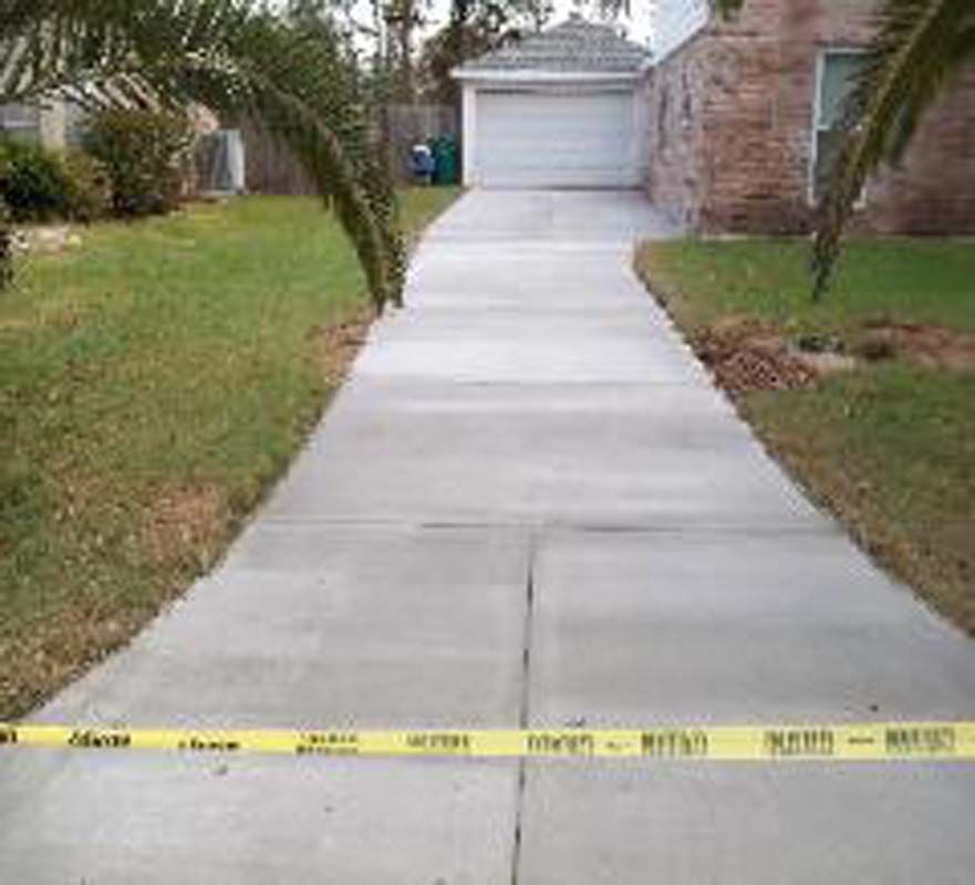 A concrete driveway leading to a house with a garage door.