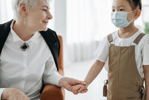 An elderly woman is holding the hand of a young girl wearing a mask.