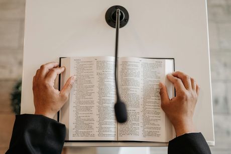 A person is reading a bible at a podium with a microphone.