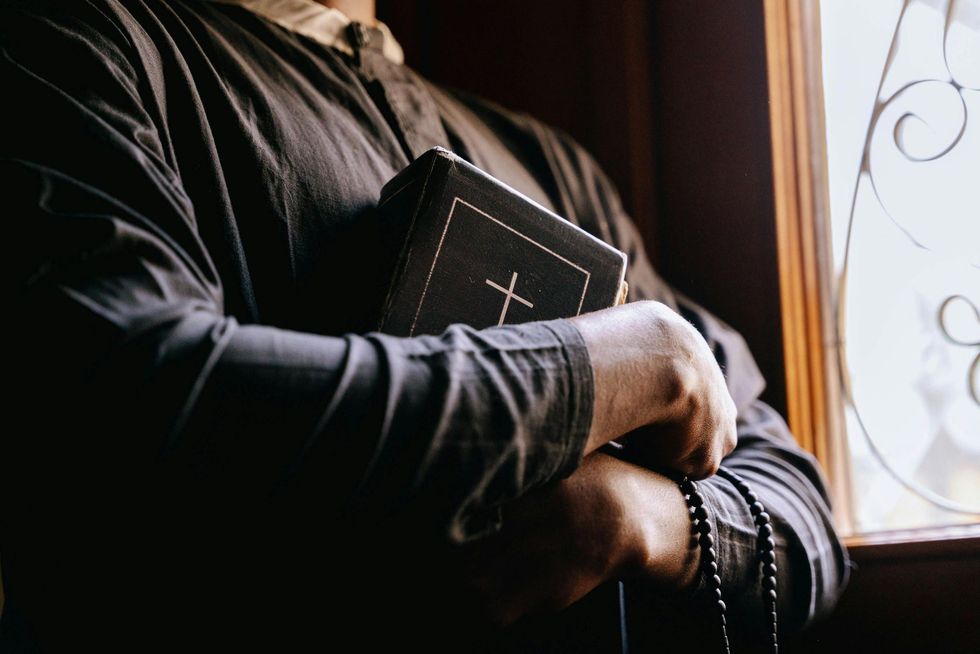 A man is holding a bible with a cross on it in front of a window.