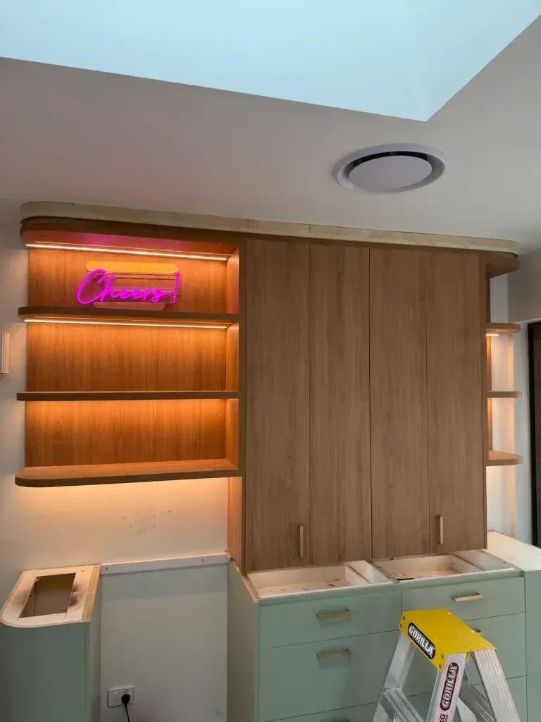 Wooden kitchen cabinets and shelves with pink neon sign, under construction.