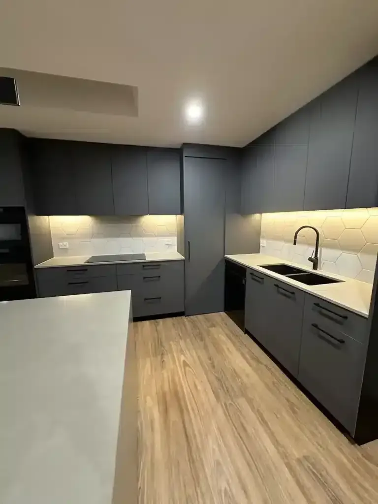 Modern gray kitchen with light wood flooring, black accents, and white countertops.