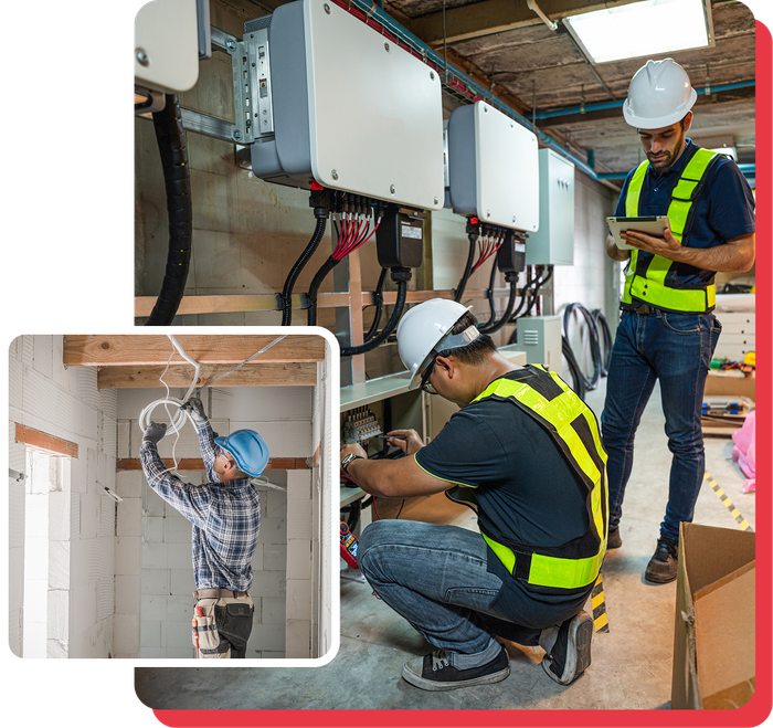 Electricians working on electrical equipment, indoor setting. One electrician is kneeling, others are observing.