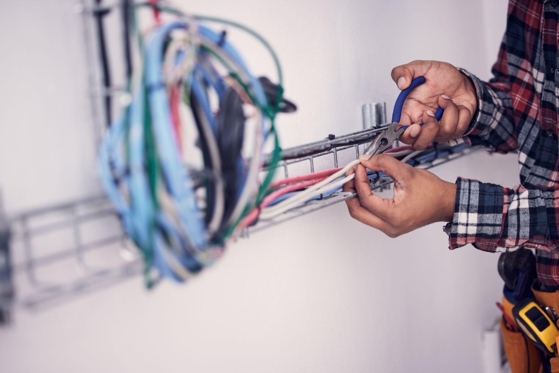 Person cutting wires with pliers near a cable rack; white wall.