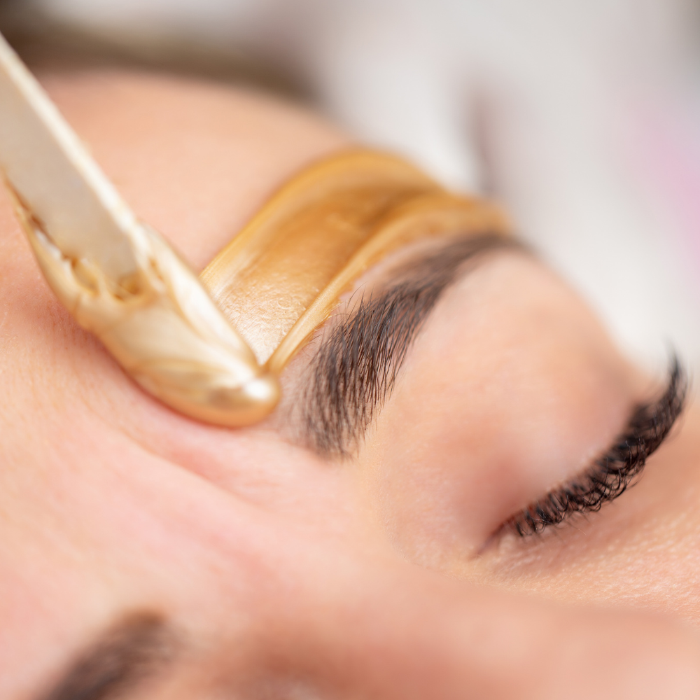 Close-up of eyebrow waxing with a spatula applying warm wax to a brow