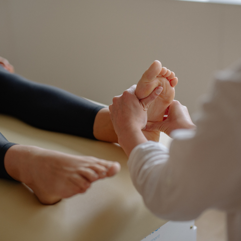 Two people gently holding hands on a soft beige surface, with a child’s feet visible nearby