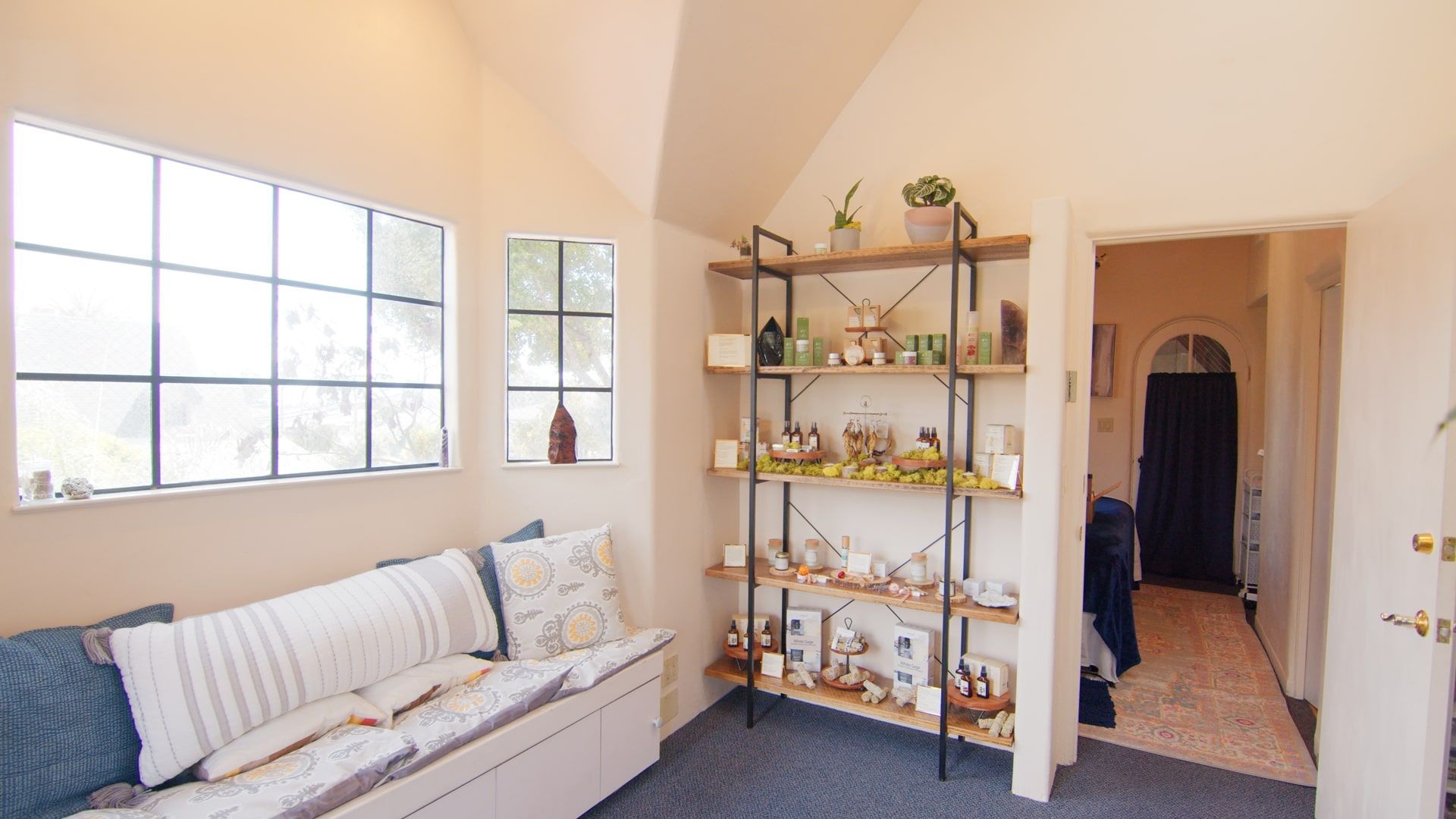 Bright living room with beige sofa, metal shelf, large window, and open doorway to hall