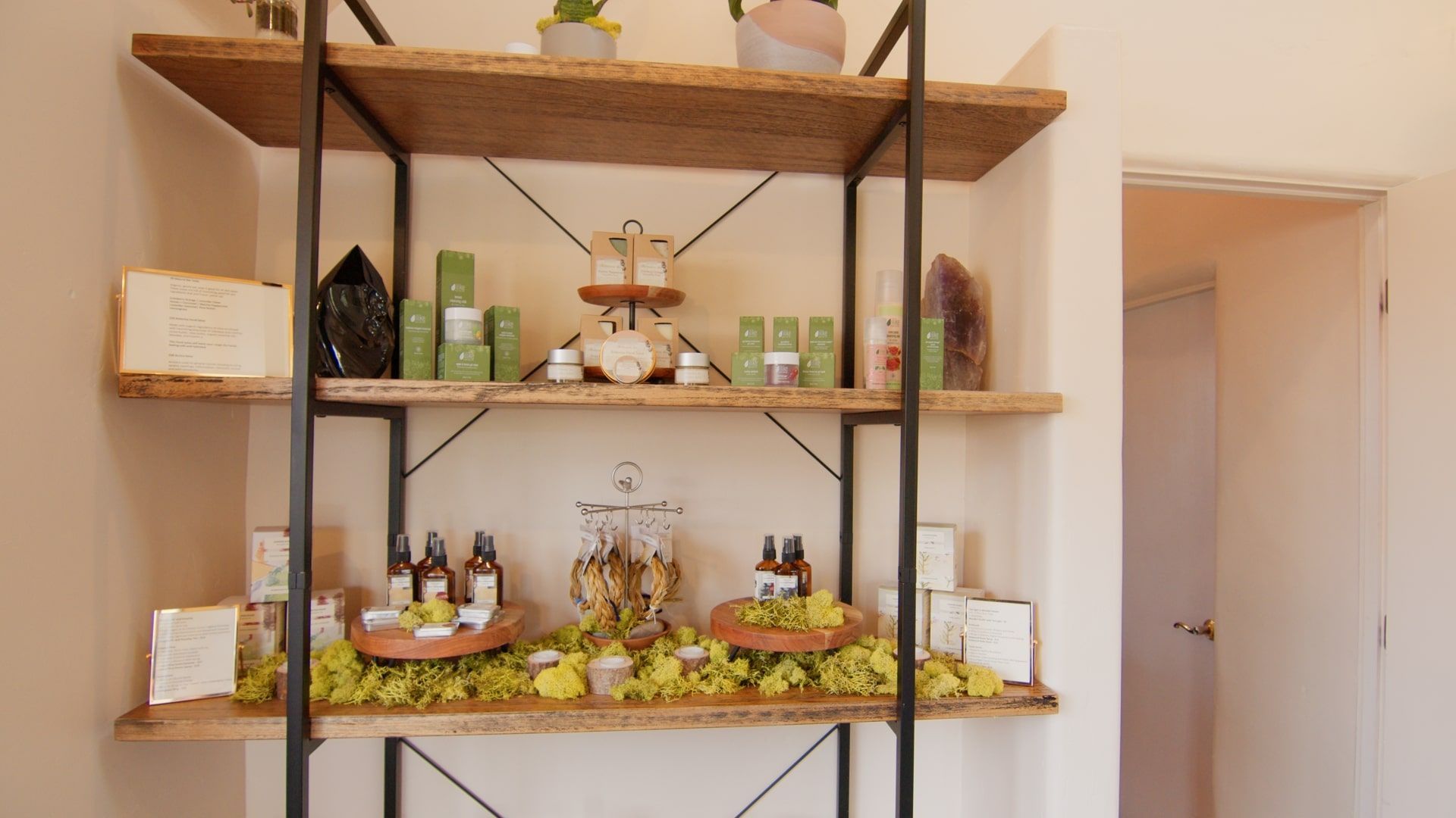 Shelves of assorted bottles and jars on a display unit in a bright room with a doorway beside it