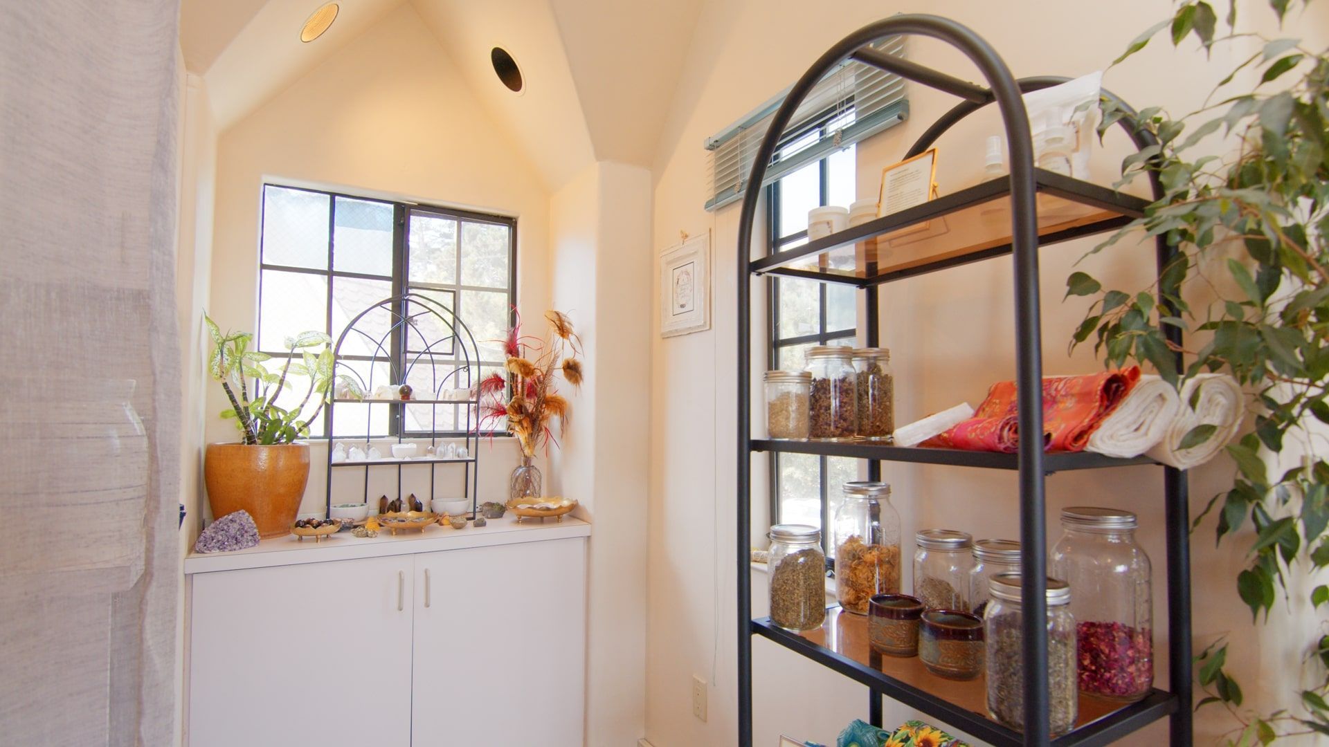 Bright kitchen nook with white cabinets, arched window, and black shelving with jars and decor.