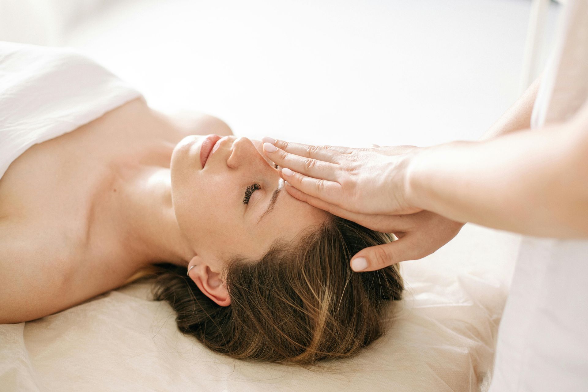 Person receiving a forehead massage while lying on a spa bed, eyes closed in a bright room