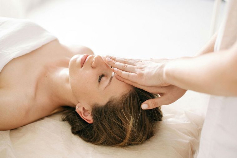 Person receiving a forehead massage while lying on a spa bed, eyes closed in a bright room