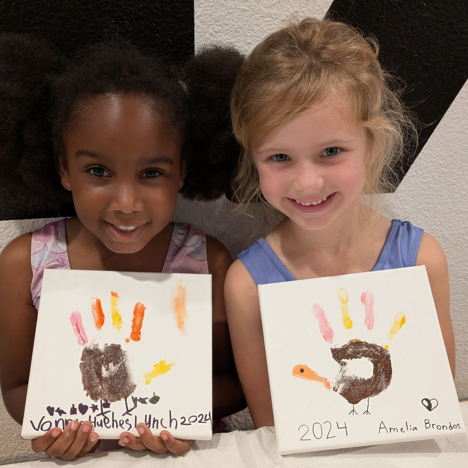 Two children smiling and holding handprint art with colorful paint on paper.