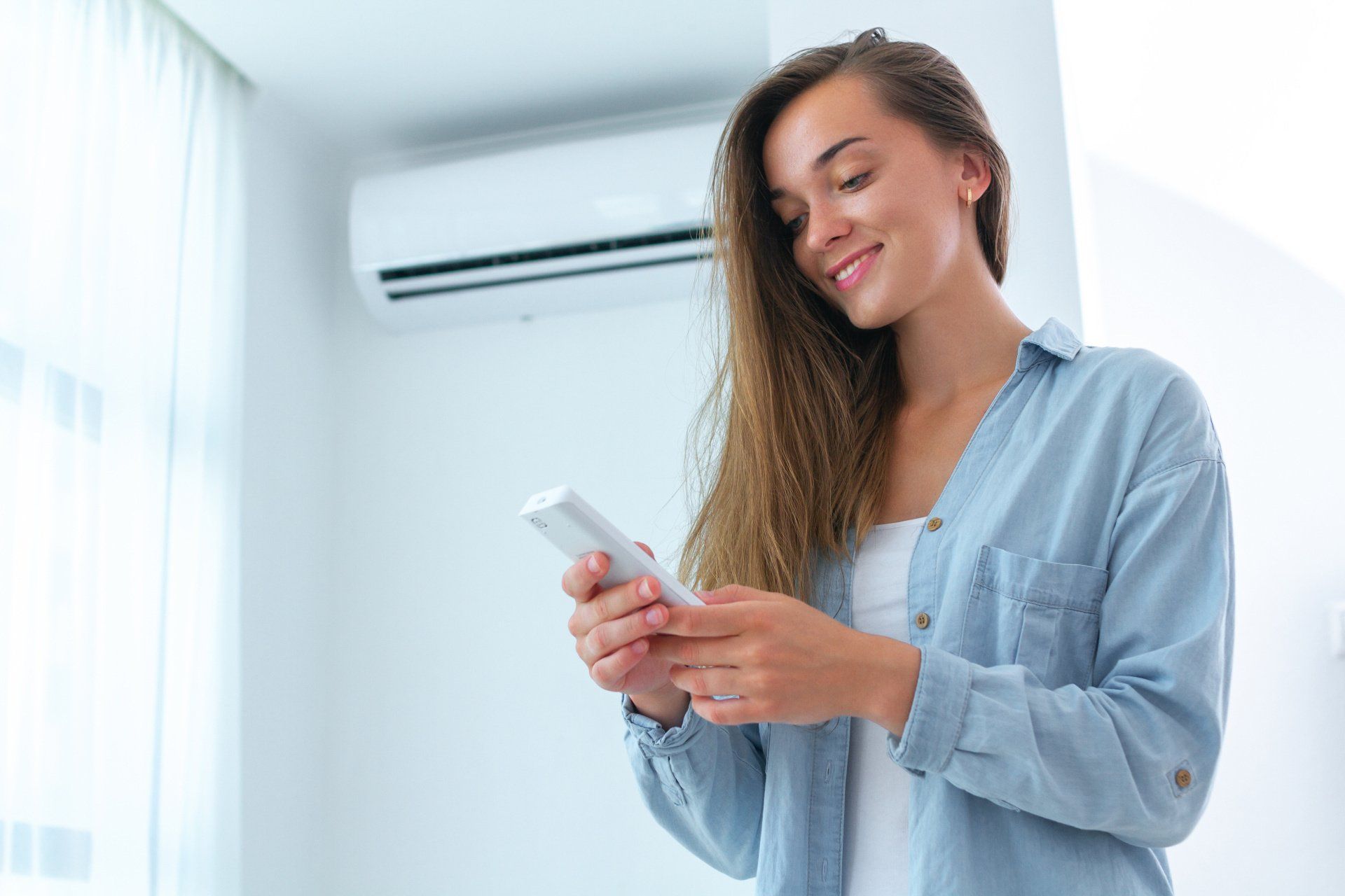 A woman is using a cell phone in front of an air conditioner.