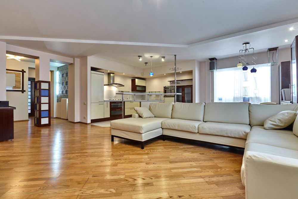 Spacious Living Room With Hardwood Floors, a White Sectional Sofa, and Open Kitchen Area — Proshield Insulation & Waterproofing In Nowra, NSW