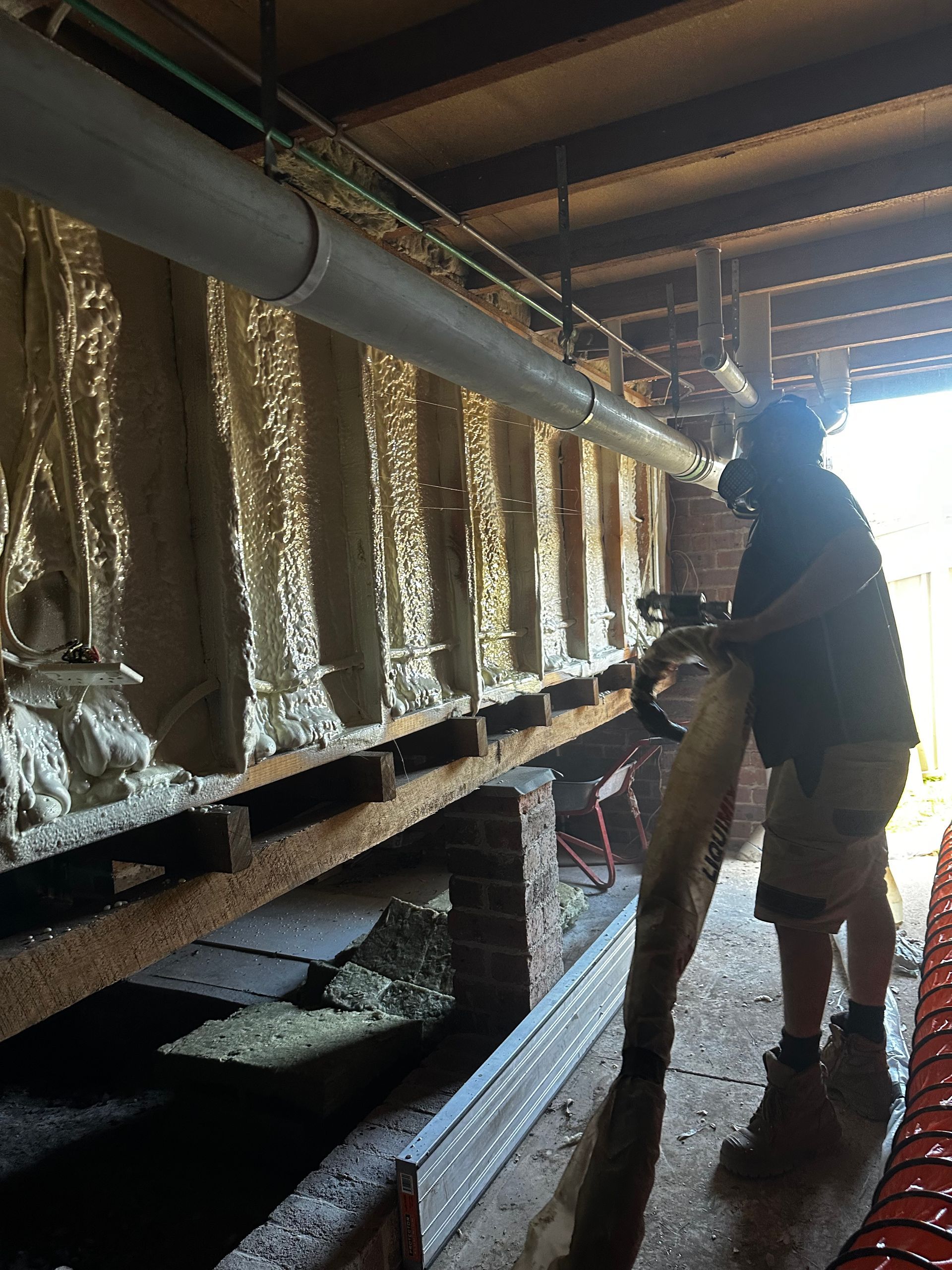 Person spraying foam insulation in crawlspace. Beige foam covers a rectangular structure  — Proshield Insulation & Waterproofing In Shell Cove, NSW