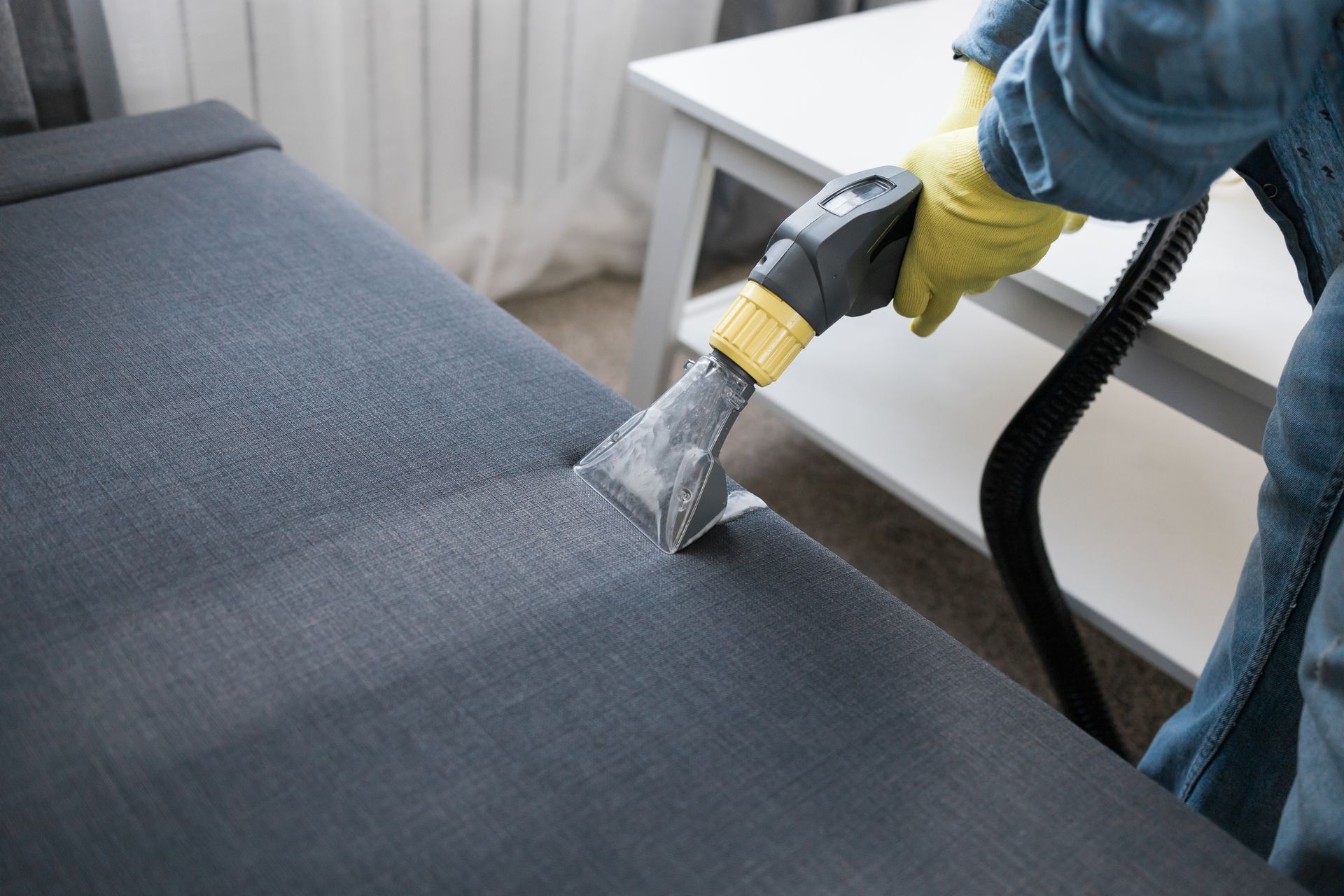 A person is cleaning a couch with a vacuum cleaner. — Durant, OK — James Dry Carpet & Upholstery Cleaning Service A person is cleaning a couch with a vacuum cleaner. — Durant, OK — James Dry Carpet & Upholstery Cleaning Service