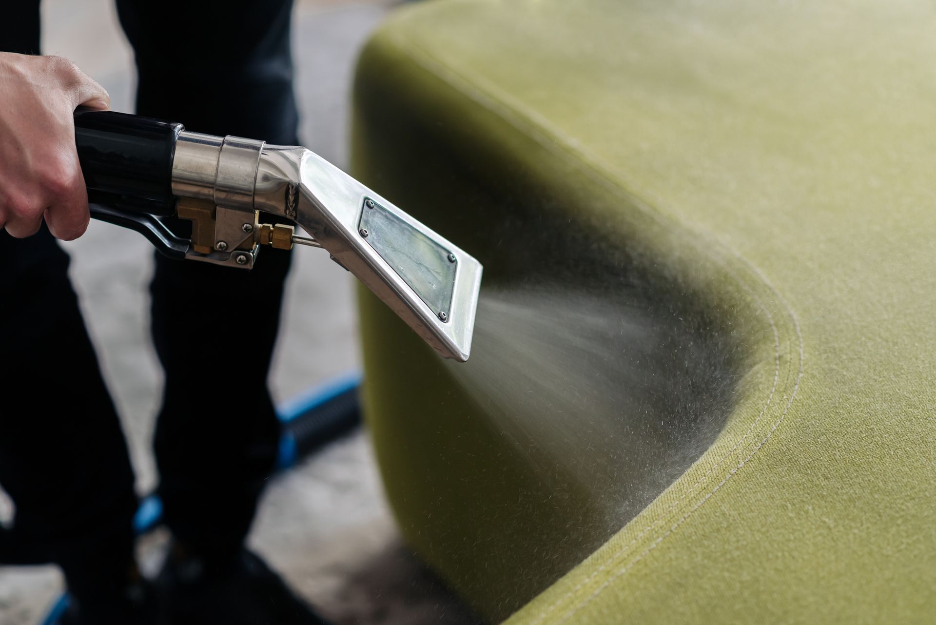A person is cleaning a green couch with a vacuum cleaner. — Durant, OK — James Dry Carpet & Upholstery Cleaning Service