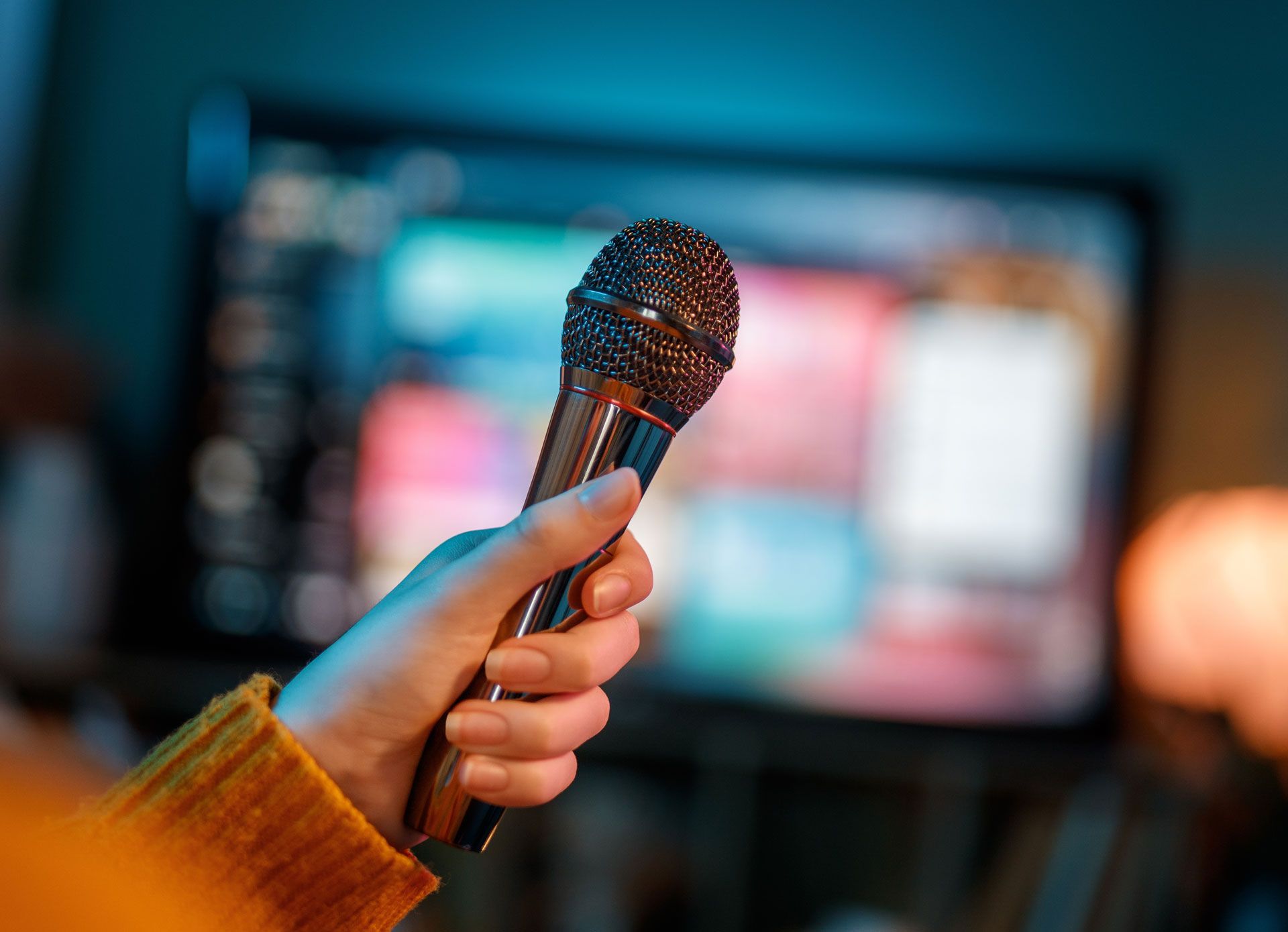 Hand holding a microphone in front of a karaoke machine screen.