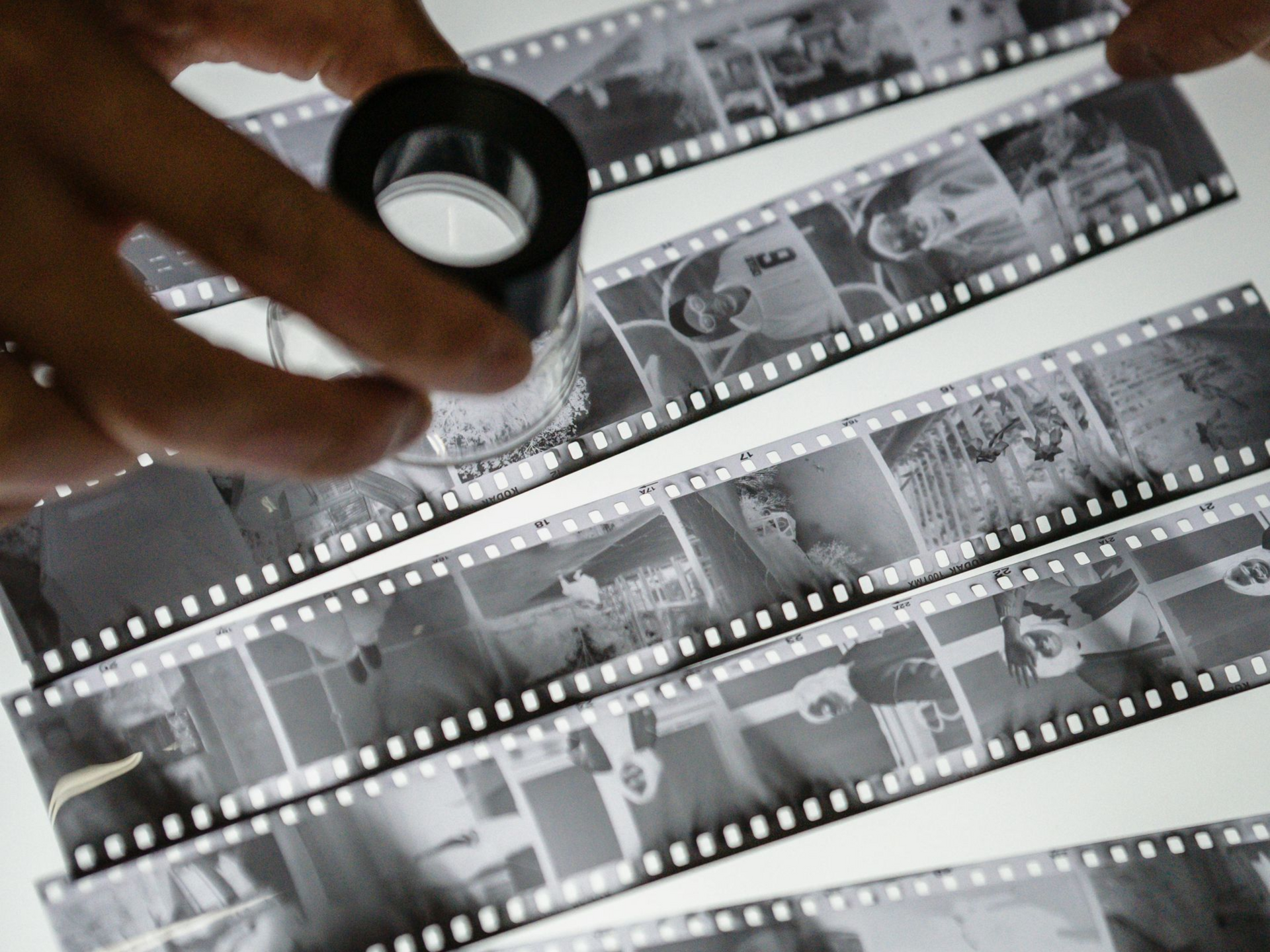 Hands examining strips of developed film with a magnifying glass on a light table.