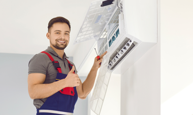 Electrician in work uniform adjusting a wall-mounted electrical panel with a screwdriver