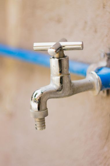Silver outdoor water faucet with a blue hose attached, mounted on a wall