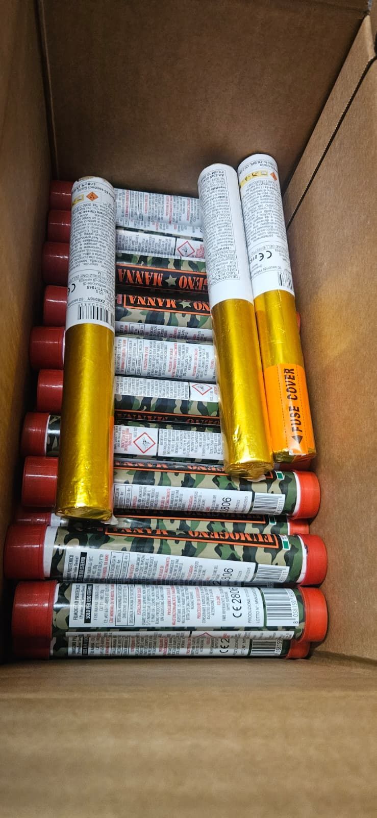 Una scatola di cartone piena di razzi cilindrici, con tappi rossi e corpi avvolti in oro e bianco.