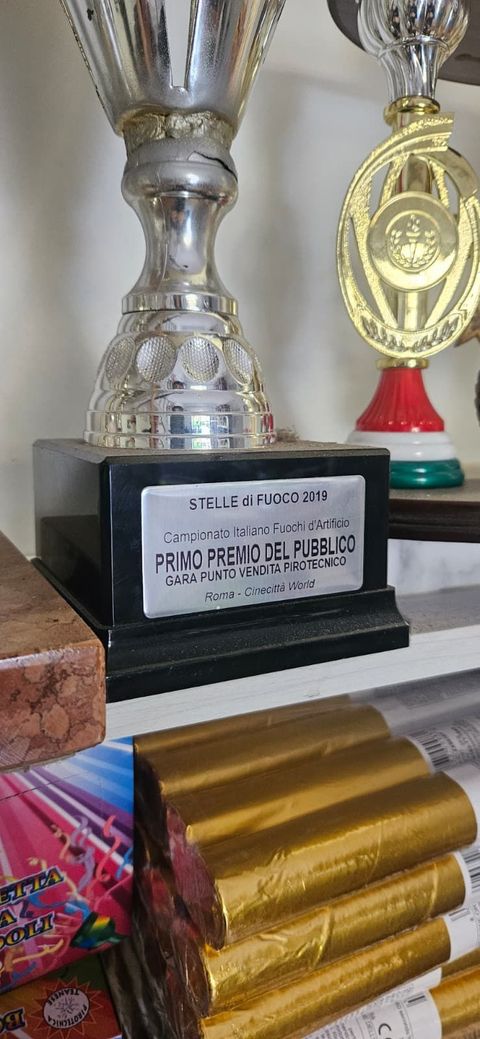Trofeo con base nera, corpo argentato e targa con testo. In primo piano, delle barrette di cioccolato.
