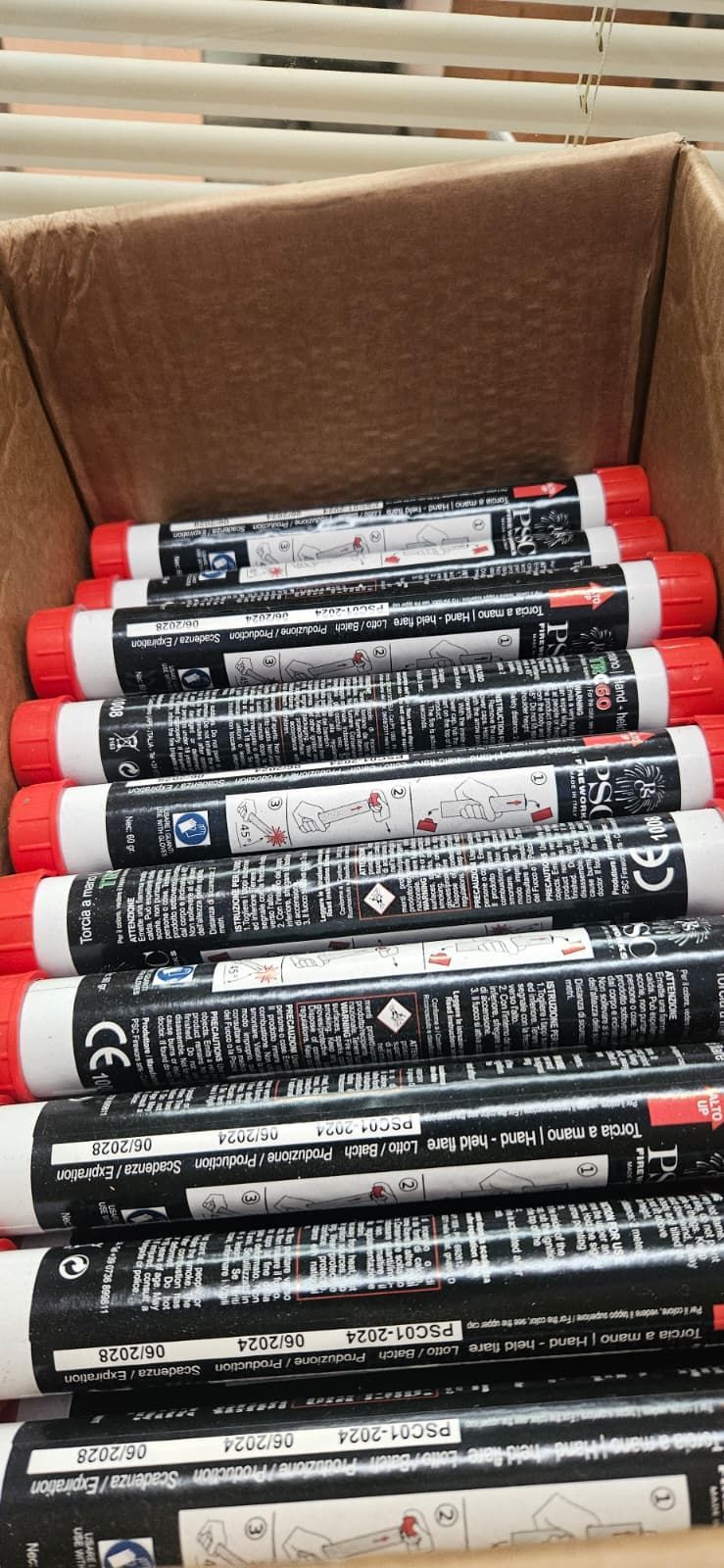 Scatola di razzi di segnalazione neri e rossi, impilati, con etichette visibili.