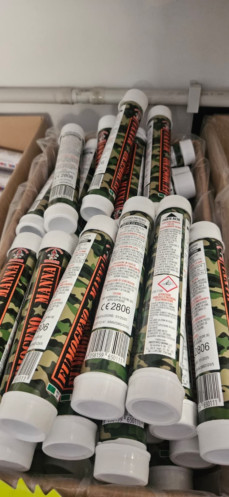 Una pila di contenitori cilindrici con tappi bianchi ed etichette con motivo mimetico, probabilmente articoli per la vendita al dettaglio.