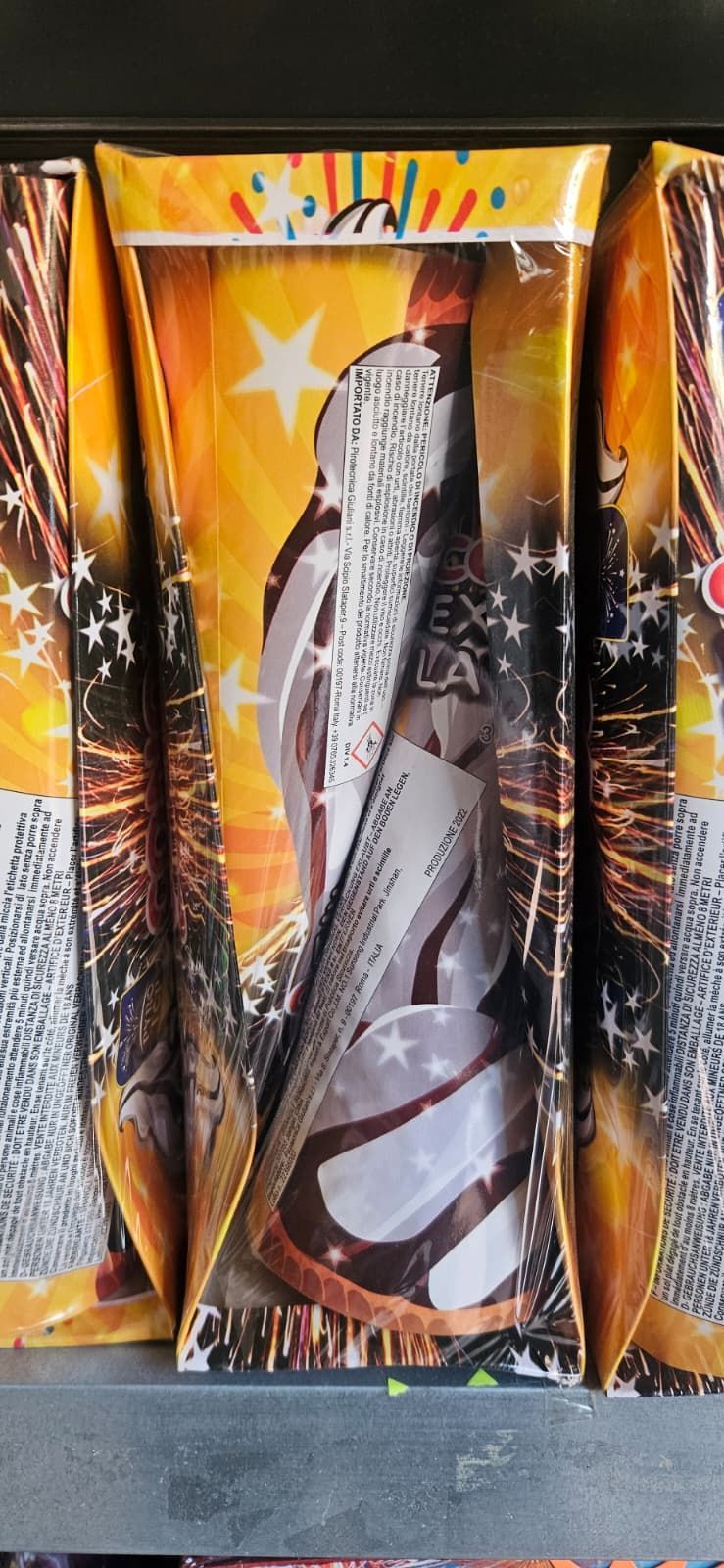 Scatole di fuochi d'artificio, raffiguranti un motivo a stella centrale, sfondo giallo e istruzioni.