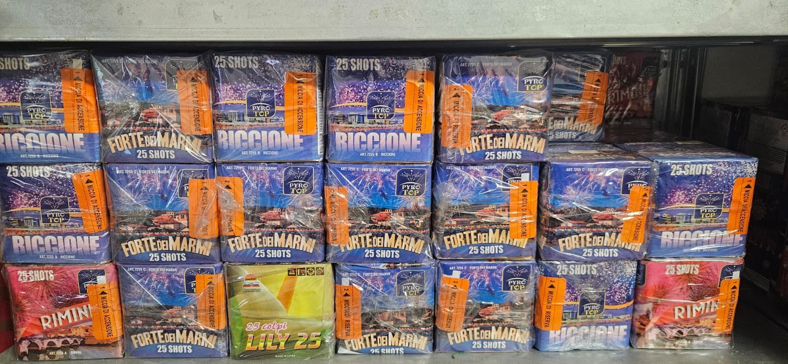 File di scatole di fuochi d'artificio con etichette arancioni, per lo più blu con immagini di fuochi d'artificio.