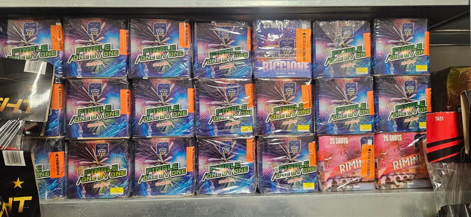 Scaffale di scatole di fuochi d'artificio con etichette arancioni, caratterizzate da vari motivi colorati.