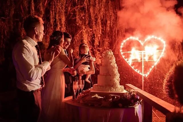 Taglio della torta nuziale con fuochi d'artificio a forma di cuore. Coppia con gli invitati.